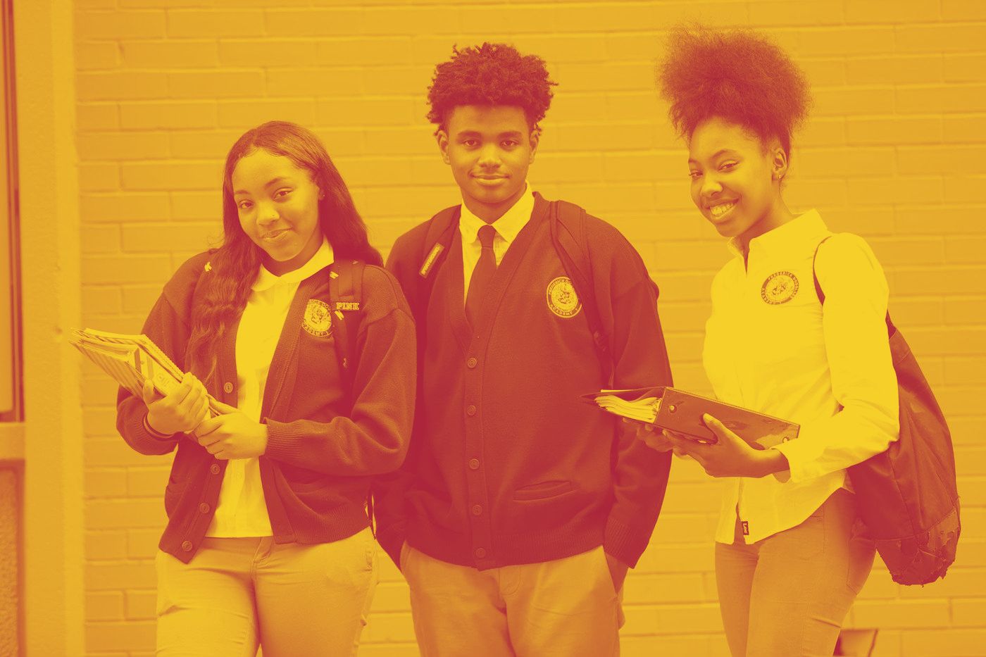 Three Frederick Douglass Academy students in crimson crested cardigans outside the school building.